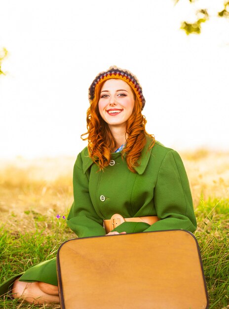 Fille rousse avec valise assis à l&#39;herbe de l&#39;automne