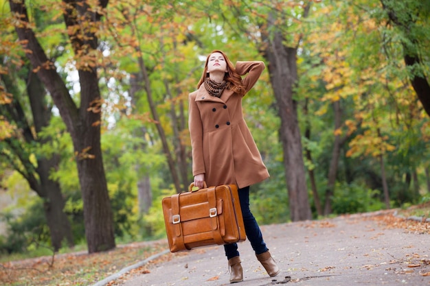 Fille rousse avec valise à l'automne en plein air