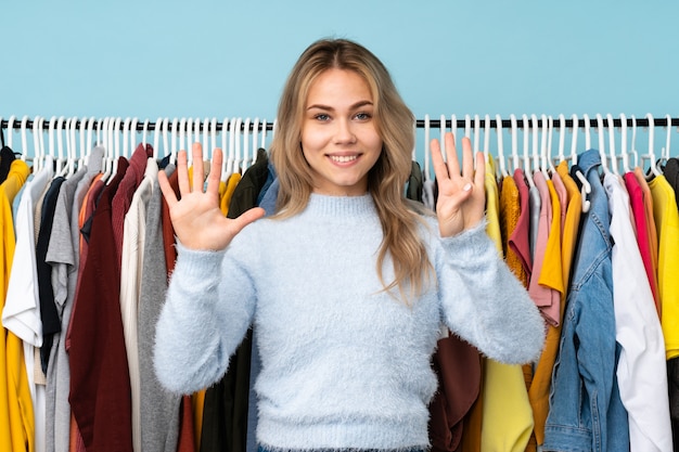 Fille russe achetant des vêtements sur le mur bleu en comptant neuf avec les doigts