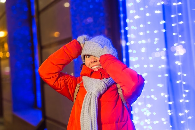 Fille s'amusant sur les lumières de décoration de noël rue jeune femme souriante heureuse portant élégant