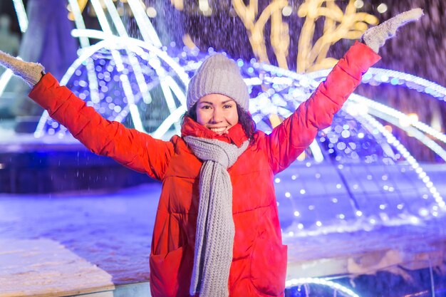 Fille S'amusant Sur La Rue Des Lumières De Décoration De Noël. Jeune Femme Souriante Heureuse Portant Une écharpe Et Une Veste Tricotées élégantes à L'extérieur. Modèle En Riant. Scène De Ville Au Pays Des Merveilles D'hiver, Fête Du Nouvel An.