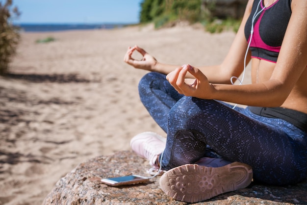 La fille s'assied dans la position de lotus sur la plage et médite le jour ensoleillé écoutant