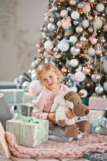 La fille s'assied près de l'arbre de Noël et étreint une poupée de loup dans la peau d'aussi