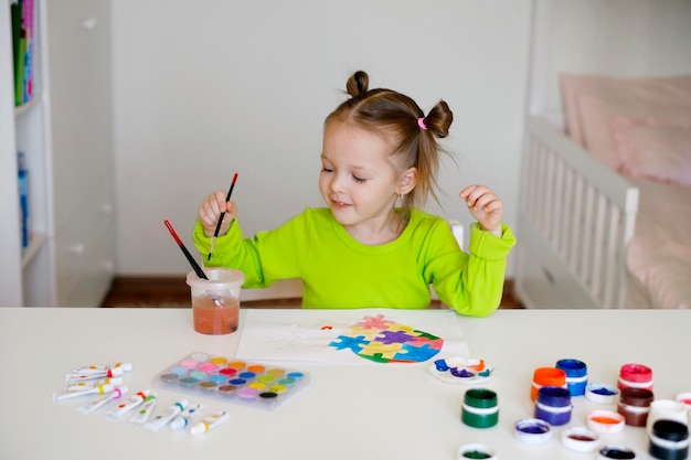 La fille s'assied à une table et dessine une image sur le thème du symbole d'autisme