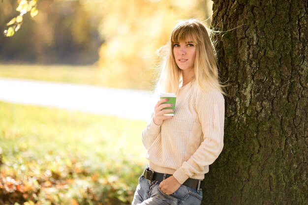 Fille s'assoit et se détend sur le sol dans la forêt d'automne avec du café