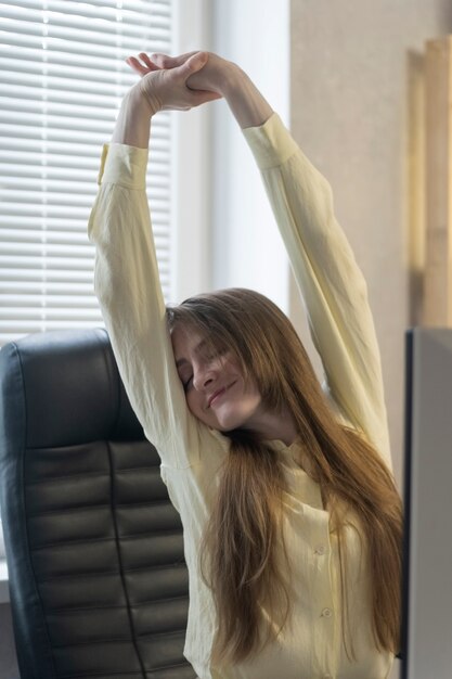 La fille s'échauffe en étant assise sur le lieu de travail. Exercices du dos pendant la pause de travail. La femme leva les bras