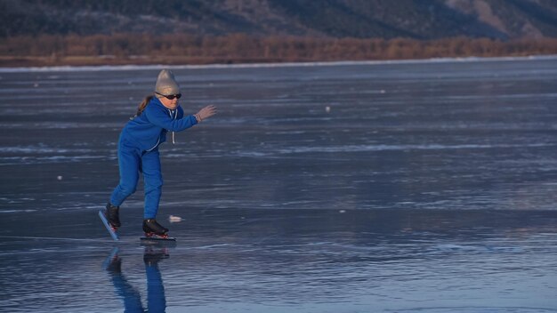 La fille s'entraîne au patinage de vitesse sur glace. L'enfant patine en hiver en costume de sport bleu, lunettes de sport. Sport de patinage de vitesse pour enfants.