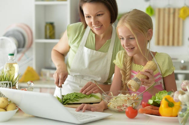 Fille avec sa mère cuisinant et regardant un ordinateur portable