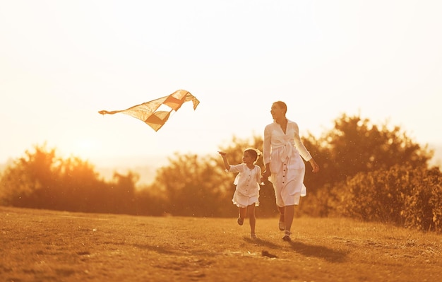 Fille avec sa mère s'amuser ensemble en courant avec un cerf-volant sur le terrain éclairé par une belle lumière du soleil