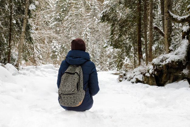 Fille avec sac à dos assis dans une forêt de conifères enneigée.