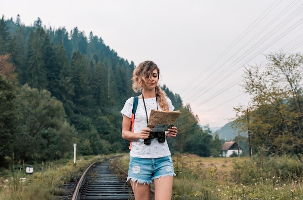 Une fille avec un sac à dos et une carte marche le long du chemin de fer