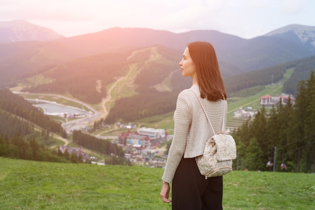 Fille avec un sac à dos debout sur la colline et admirant les montagnes. Ville au loin