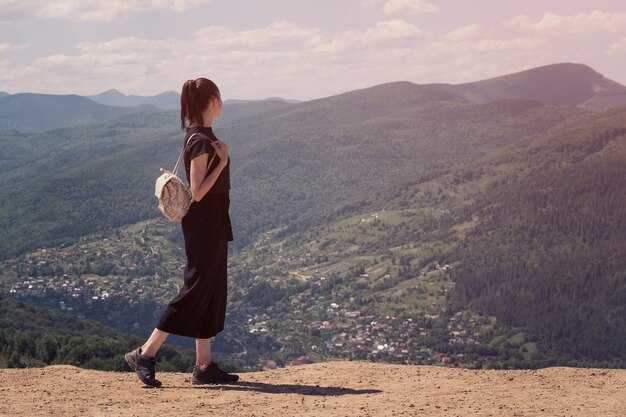 Fille avec un sac à dos debout sur la colline et admirant la vue. Journée ensoleillée