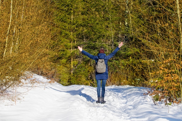 Fille avec un sac à dos est debout avec les bras levés dans une forêt enneigée