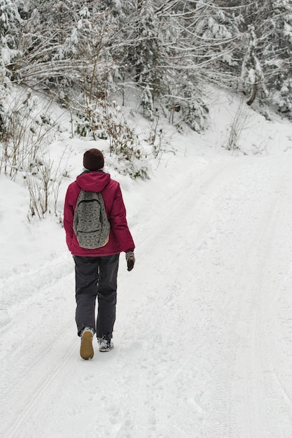 Fille avec un sac à dos marchant le long de la route dans une forêt enneigée Jour d'hiver