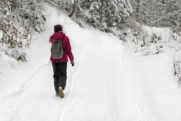 Fille avec un sac à dos, marchant le long de la route dans une forêt enneigée.