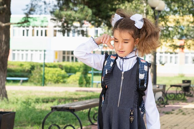 Fille avec un sac à dos près de l'école après les cours mécontente fatiguée et mal de tête L'enfant pleure en tenant sa tête dans ses mains Échecs scolaires mauvaises notes surmenage