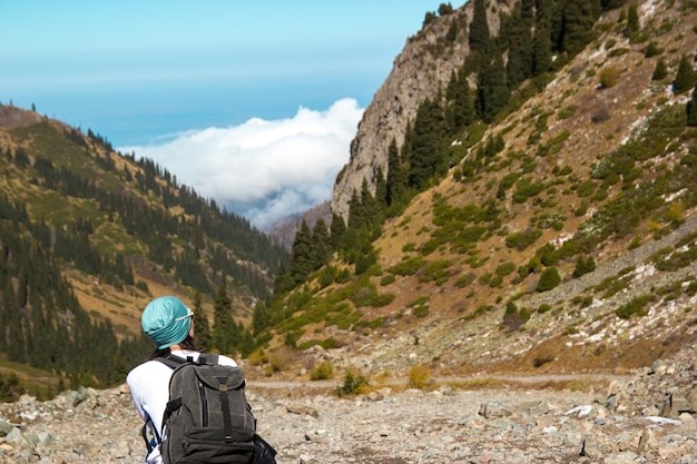 Une fille avec un sac à dos se repose parmi les hautes montagnes. La gorge avec des nuages.