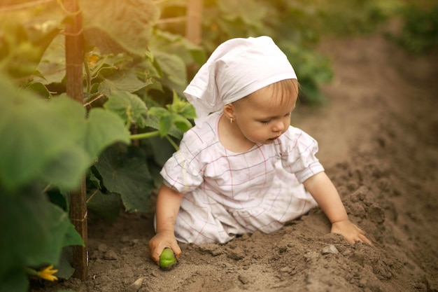 Une fille sale non lavée vêtue d'une robe et d'un mouchoir rampe dans un champ et creuse dans le sol
