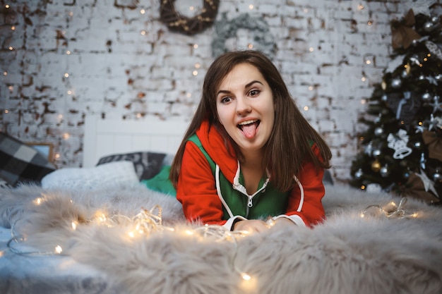 Une fille en salopette du Nouvel An avec une ambiance festive est allongée sur un lit autour de guirlandes lumineuses