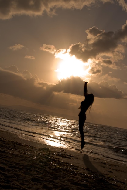 Fille sautant sur le lever du soleil à la plage