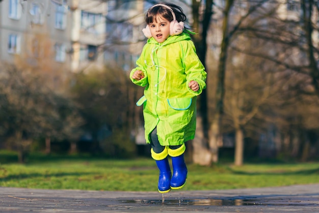 fille saute sur les flaques d'eau dans un imperméable vert