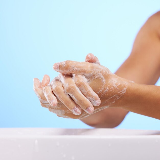 Fille de savon ou se laver les mains en studio sur fond bleu pour le bien-être ou une hydratation saine des soins de la peau Maquette de soins de santé zoom sur les soins du corps ou femme nettoyant avec un liquide pour l'hygiène ou la prévention des bactéries