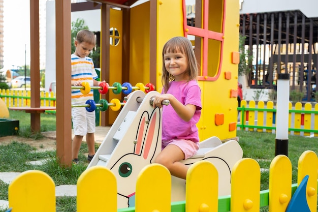 La fille se balance dans une chaise berçante en bois sur un ressort un garçon joue avec des anneaux en bois colorés