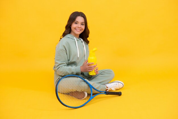 Fille se détendre après l'entraînement sportif. dédié à la remise en forme. joueur de tennis ou de badminton. adolescent avec bouteille d'eau de sport. enfance heureuse. enfant gai en tenue de sport raquette. enfant avec raquette.