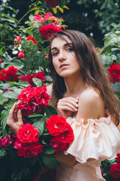 Fille se dresse contre un mur de buissons avec des roses rouges