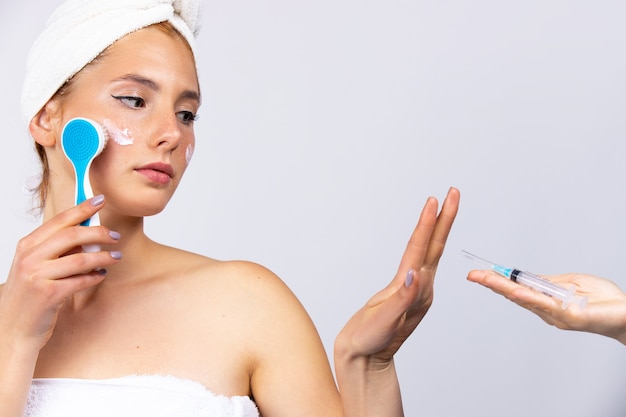 La fille se fait un massage avec une brosse cosmétique et refuse pensivement les injections cosmétiques. Photo avec un espace vide. Photo de haute qualité