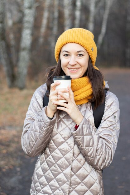 Une fille se promène dans le parc en automne avec une tasse de café