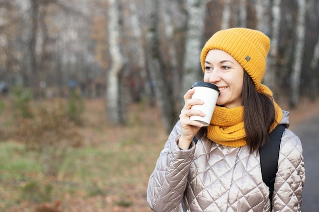 Une fille se promène dans le parc en automne avec une tasse de café