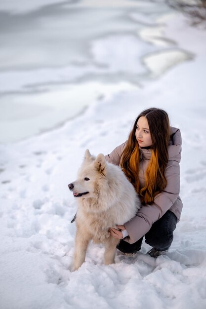 Une fille se promène avec son animal de compagnie Samoyed en hiver sur le rivage d'un lac dans le parc