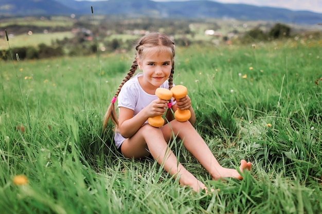 Fille se reposant sur l'herbe verte après ses exercices matinaux avec haltère dans les montagnes