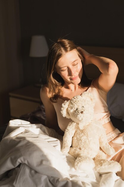 La fille se réveille le matin s'étire dans son lit et le soleil brille de la fenêtre Heureuse jeune femme accueille une nouvelle journée ensoleillée