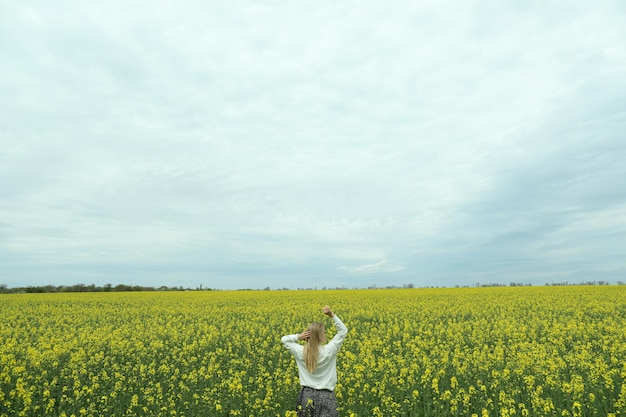 Une fille se tient dans un champ de colza un jour d'été