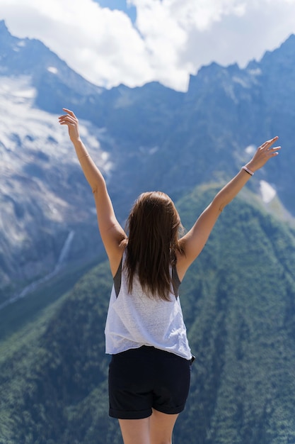 Une fille se tient dans les montagnes et lève les mains vers le ciel.