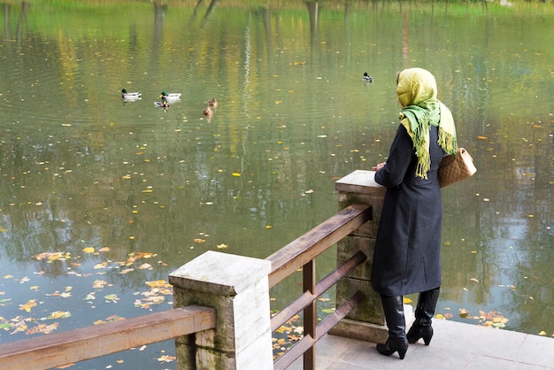 Une fille se tient sur un pont et regarde vers la rive opposée le jour de l'automne