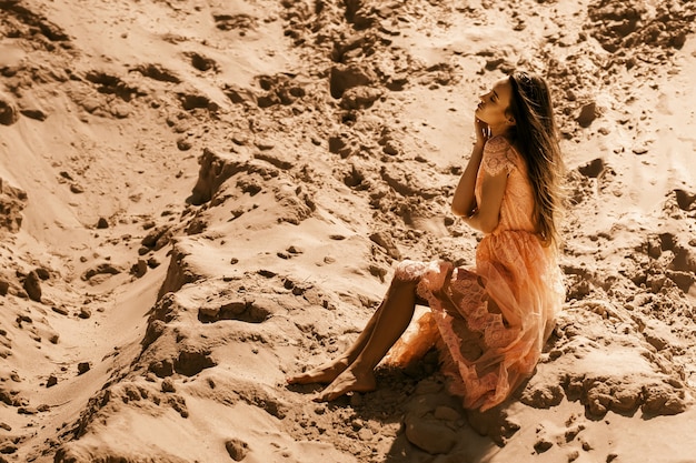 Une fille sensuelle est assise sur un sable avec les yeux fermés dans un désert