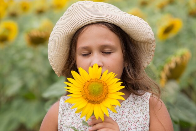 Fille sentant le tournesol dans le champ d'été à jour nuageux