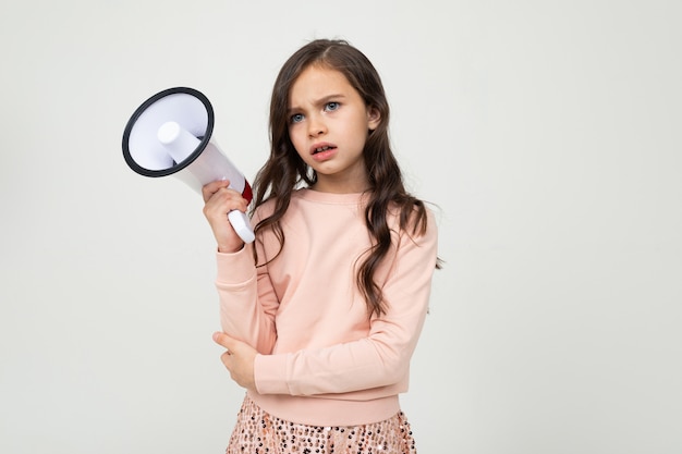 Fille sérieuse européenne avec un mégaphone sur un mur de studio blanc avec espace vide