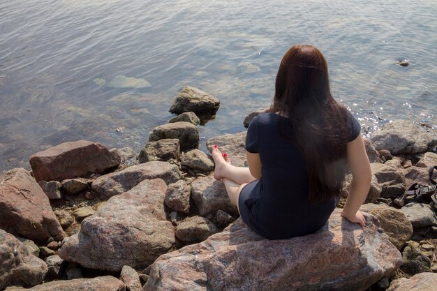 Fille seule assise sur la côte de pierre et regardant la mer