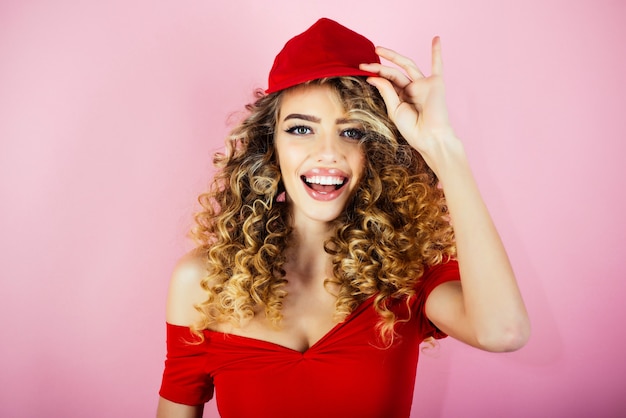 Fille sexy aux cheveux bouclés en bonnet rouge. Métier de l'industrie de la beauté et de la mode. Maquillage et cosmétiques pour les soins de la peau. Beauté et style. Vêtements à la mode. Isolé sur fond rose.