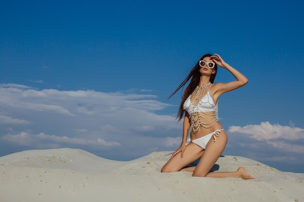 Fille sexy dans le sable en bikini blanc