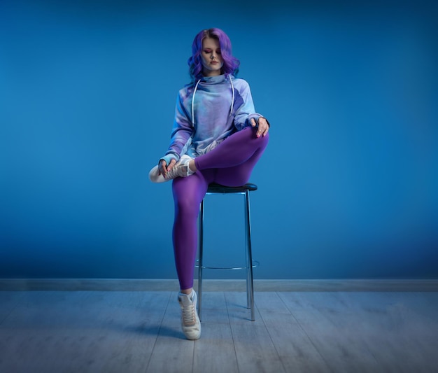 Fille sexy dans des vêtements de sport brillants pour les jeunes et des poses sexy de cheveux violets sur un fond clair