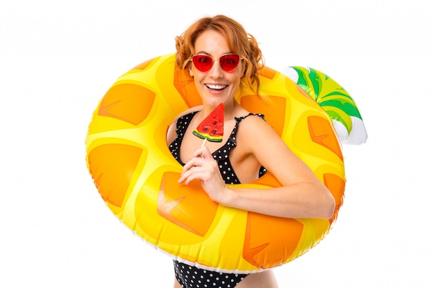 Fille sexy en maillot de bain dans un cercle de natation en forme d'ananas en vacances sur fond blanc
