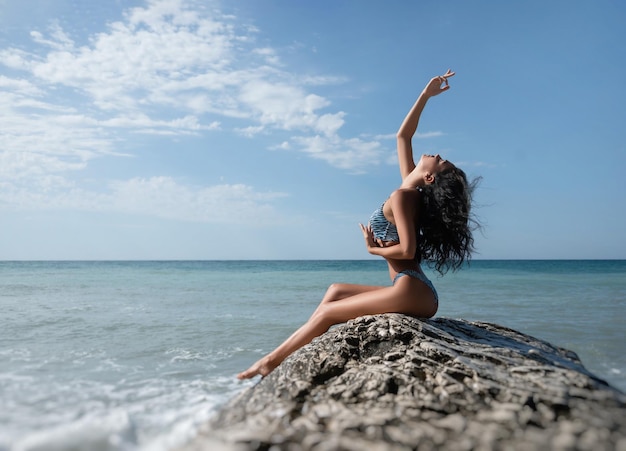 Une fille sexy en maillot de bain pose svelte sur un rocher blanc sur fond de mer