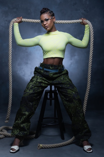 Photo fille sexy portant un pantalon de style militaire et des sous-vêtements néon posant avec une corde et regardant dans la caméra en studio