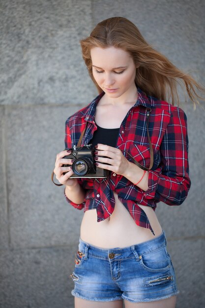 Fille en short et chemise rouge dans une cage, avec un appareil photo rétro dans les mains